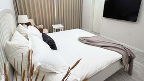 A modern hotel room with a large bed, a flat-screen TV, a small table, and a ceiling light.