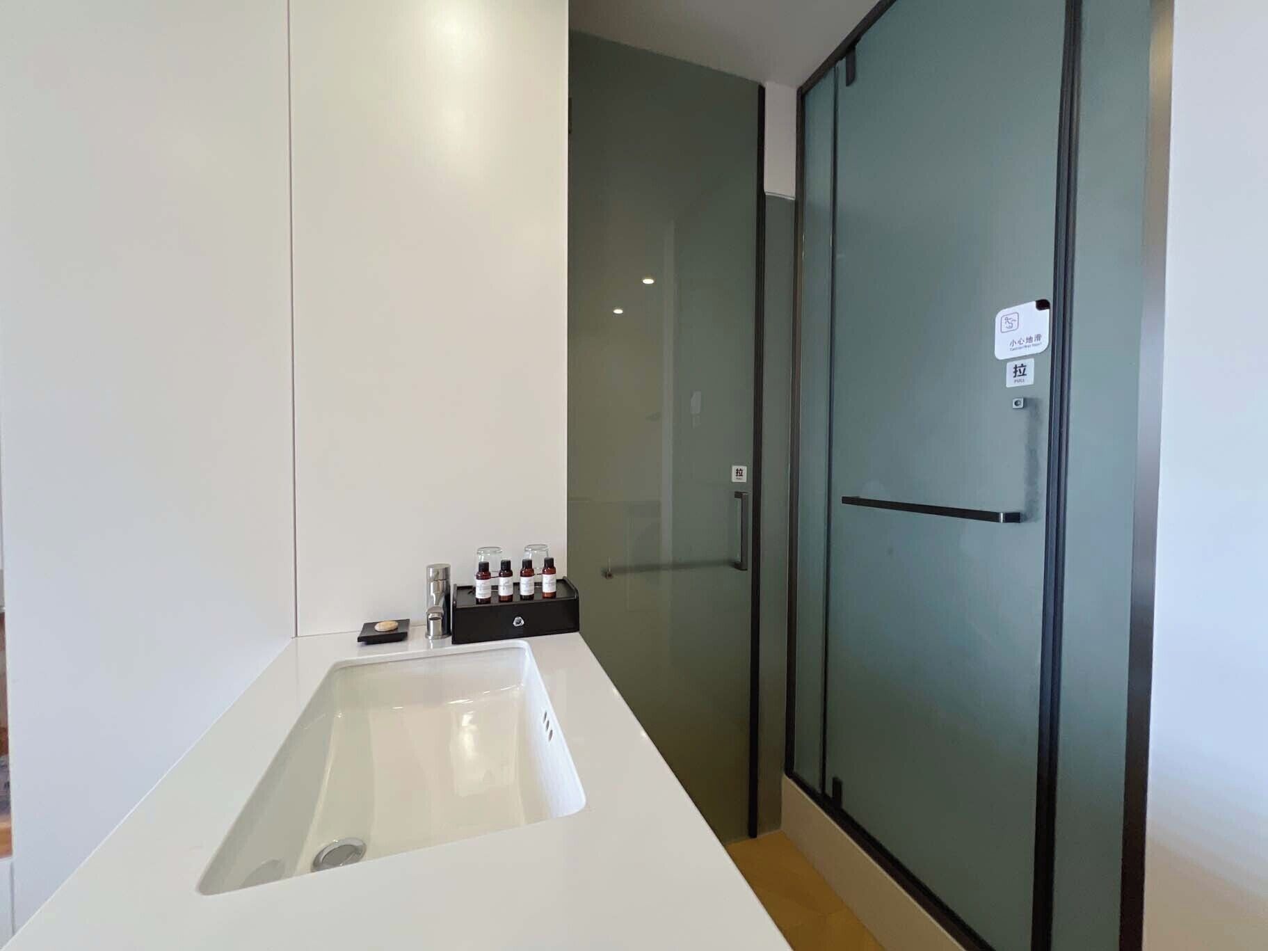 Une salle de bain moderne avec un lavabo blanc, une cabine de douche en verre et une porte en verre dépoli.