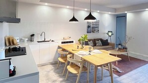 A modern kitchen with a central island, wooden dining table, and chairs. There is a built-in oven, a sink, and a stove. The room has a contemporary design with a blue accent wall and a ceiling light fixture.