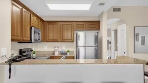 A modern kitchen with wooden cabinets, stainless steel appliances, a central island with bar stools, and a skylight. - Trendy lake condo-fireworks view (Orlando)