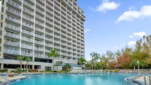 A large hotel with a swimming pool, multiple balconies, and palm trees. - Trendy lake condo-fireworks view (Orlando)