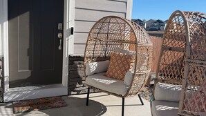 Un porche à l'avant de la maison, avec une porte sombre, des fauteuils en osier et un paillasson.