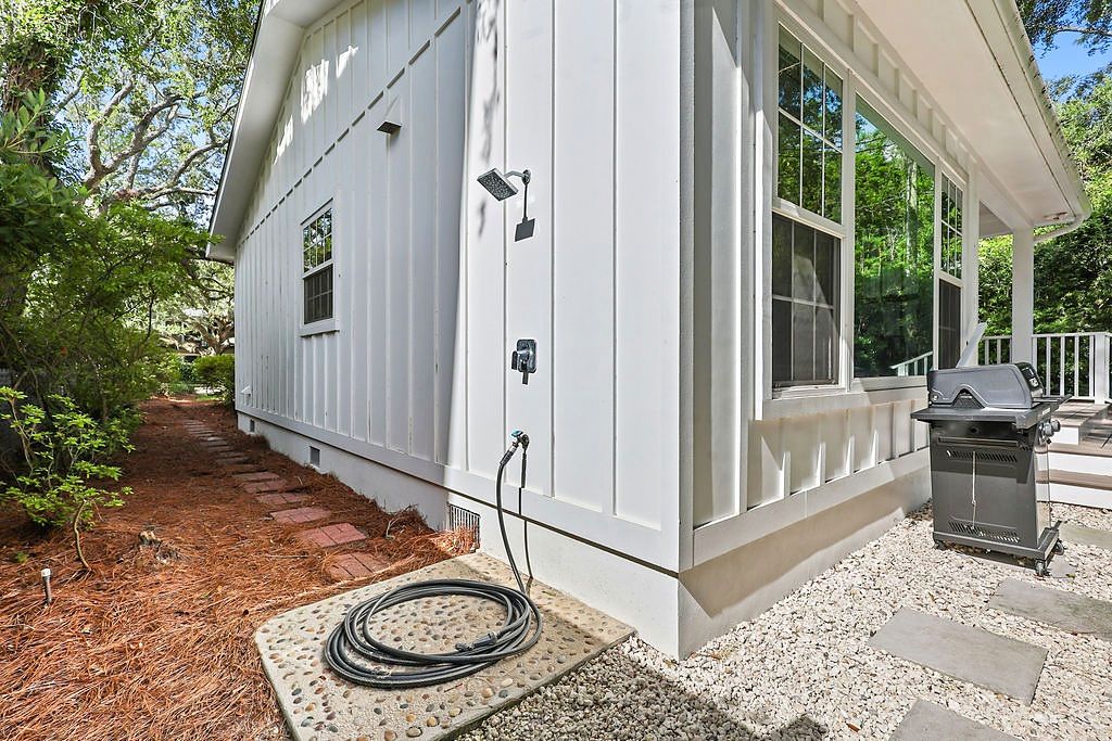 A white house with a covered porch, a grill, and a hose connected to the house.