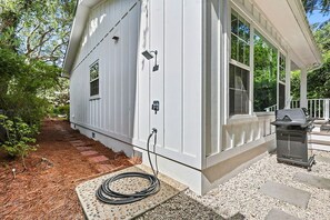 A white house with a covered porch, a grill, and a hose connected to the house. - Dog Friendly, 5-bedroom Home on East Beach, 100 Yards to Beach Access, Perfect for Family Getaways! (Saint Simons Island)