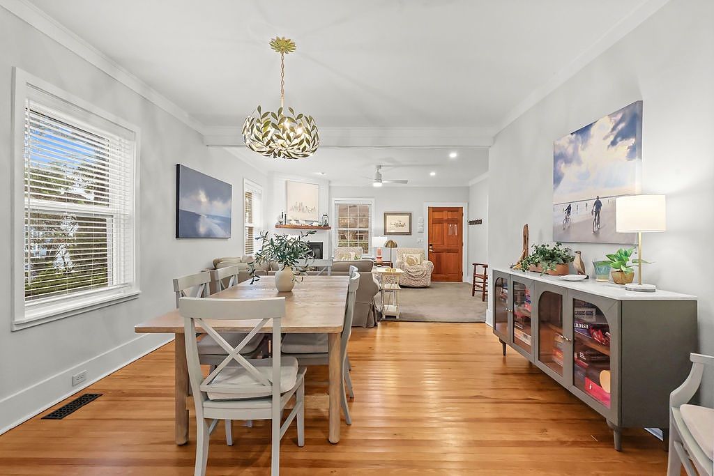 A spacious living room with a dining area, a chandelier, and a large window with blinds.