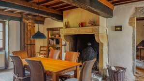 A rustic dining area with a wooden table and wicker chairs, a bookshelf, and a fireplace with a decorative mantle. - Le Moulin Mathy - SAINT PIERRE LE VIEUX (SAINT PIERRE LE VIEUX)