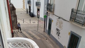 A narrow street with a white building featuring a balcony with a metal railing. - ✨ Independent Stay: King Bed, Private Bathroom and Netflix (Faro)
