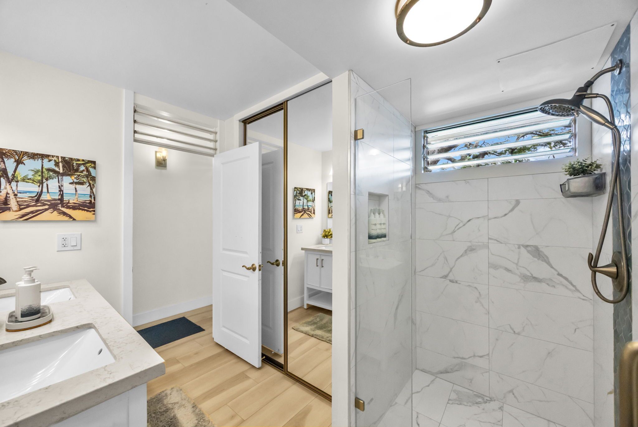 Ein modernes Badezimmer mit einer Marmerdusche, einem weißen Waschbecken und einer Tür zu einem Badezimmer mit Toilette und einem kleinen Schrank.