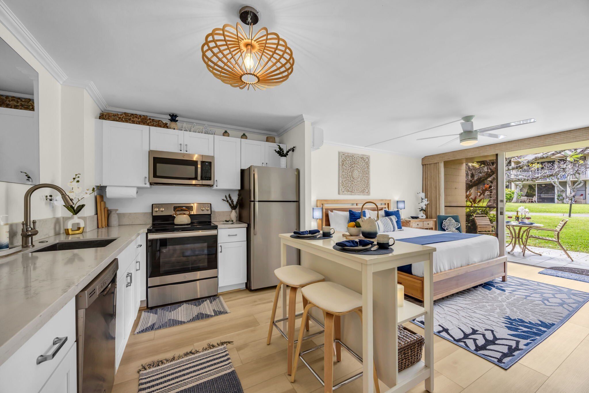 A compact kitchen with modern appliances, a dining area with stools, and a bedroom with a large bed and a view of the garden.