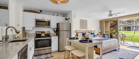A compact kitchen with modern appliances, a dining area with stools, and a bedroom with a large bed and a view of the garden.