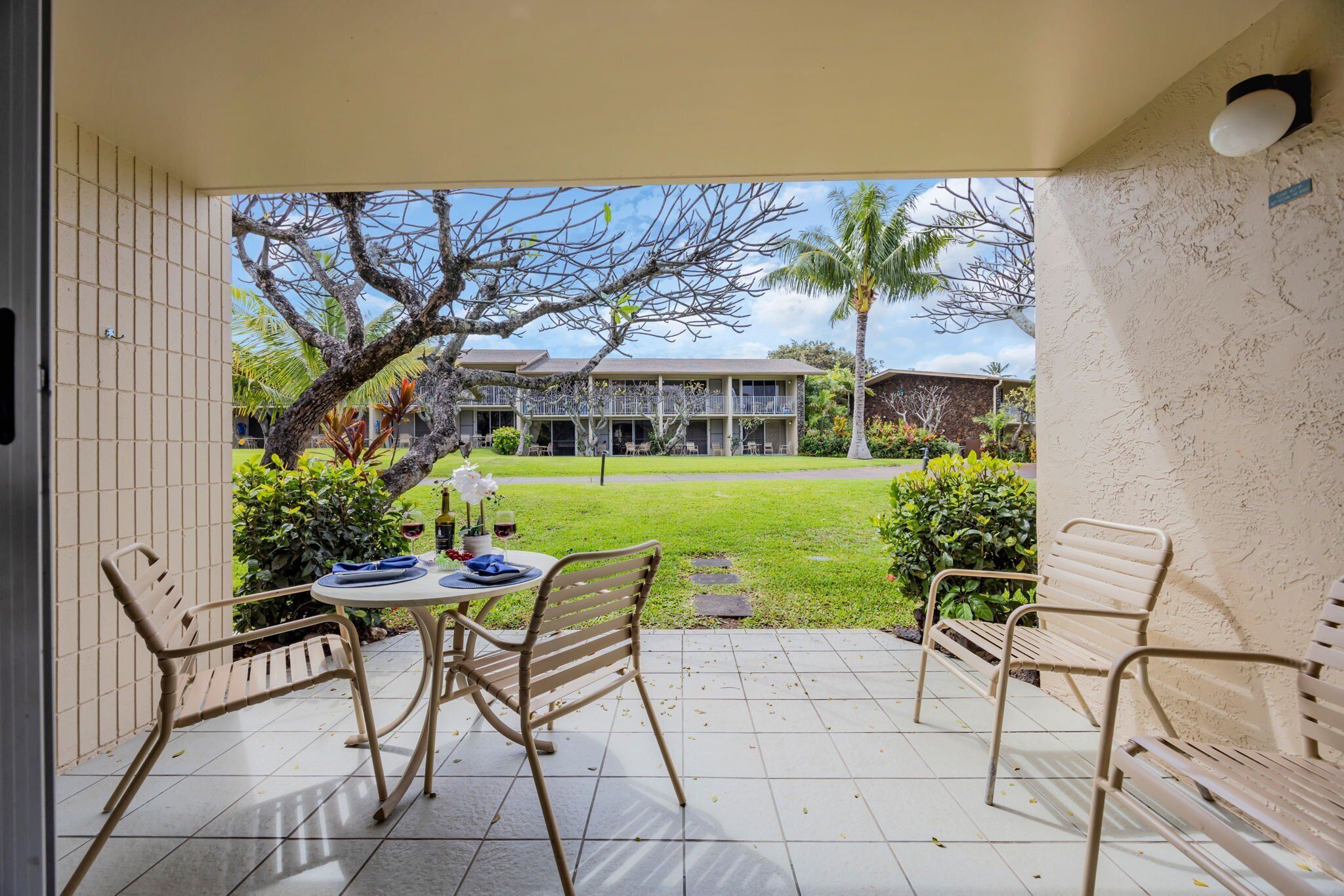 Une terrasse extérieure avec une table et des chaises, une vue sur une maison et un palmier.