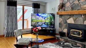 A living room with a TV, fireplace, and a view of a deck. - Charming Lakeview Cottage | Algonquin Shores (Dwight)