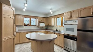 A modern kitchen with wooden cabinets, a central island, stainless steel appliances, and a window providing natural light. - Charming Lakeview Cottage | Algonquin Shores (Dwight)