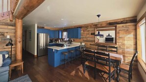 A spacious kitchen with a central island, blue cabinets, and a dining area with wooden furniture. - Golf Course Getaway w/ Patio, Near Beach & Skiing (McCall)