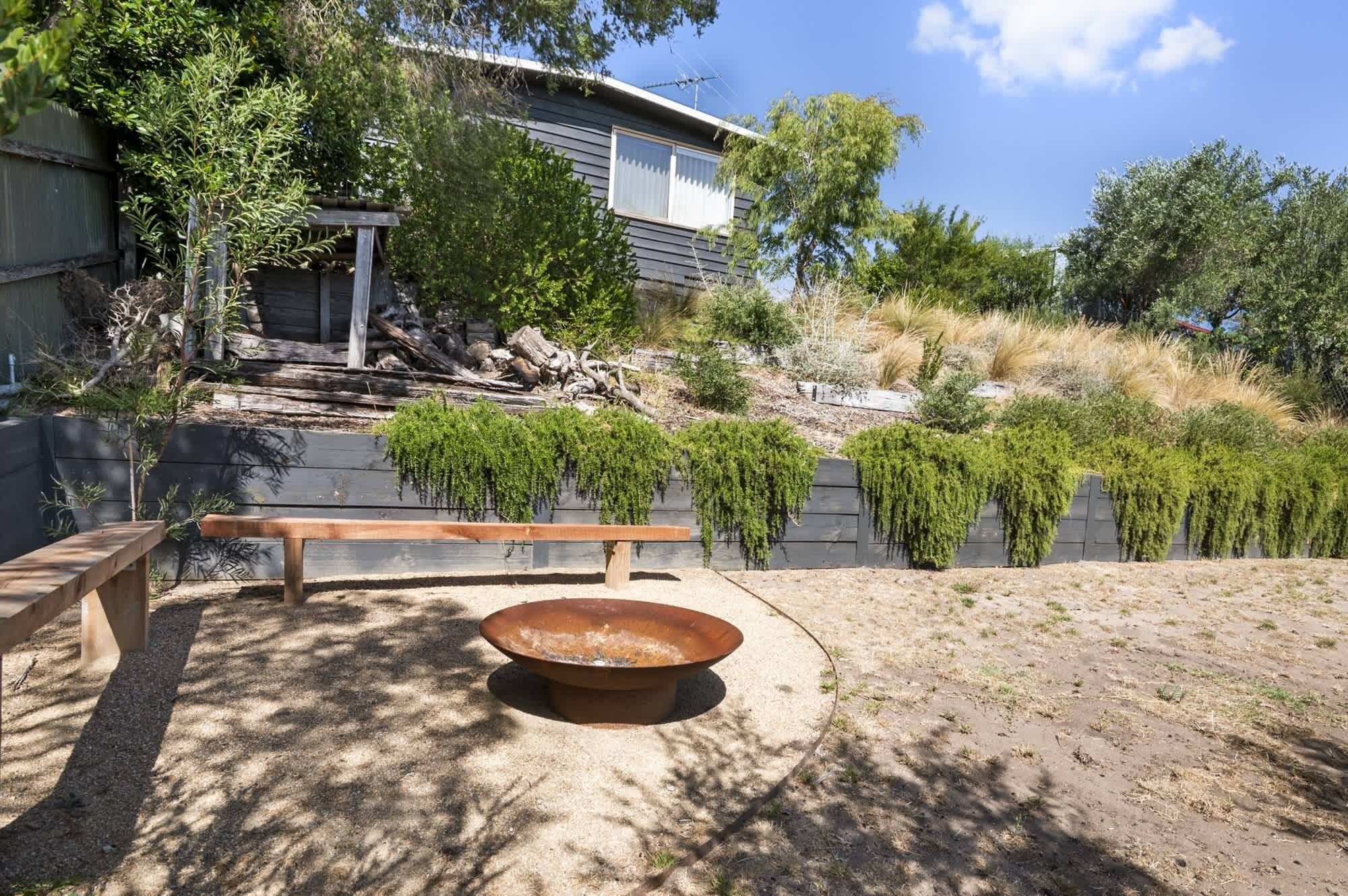 A backyard with a fire pit, wooden bench, and a house with a sloped roof.