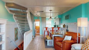 A cozy interior with a staircase, a dining area with chairs, a leather sofa, and a kitchen in the background. - Pleasure Island Treasure Is an oceanfront townhome in a perfect location! (Carolina Beach)