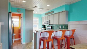 A kitchen with teal walls, white cabinets, and a central island with orange bar stools. - Pleasure Island Treasure Is an oceanfront townhome in a perfect location! (Carolina Beach)