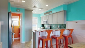 A kitchen with teal walls, white cabinets, and a central island with orange bar stools. - Pleasure Island Treasure Is an oceanfront townhome in a perfect location! (Carolina Beach)