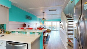 A kitchen with a central island, a dining area with red chairs, and a staircase leading to an upper level. - Pleasure Island Treasure Is an oceanfront townhome in a perfect location! (Carolina Beach)