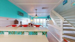 A kitchen with a white island, red chairs, and a staircase with a white railing. - Pleasure Island Treasure Is an oceanfront townhome in a perfect location! (Carolina Beach)