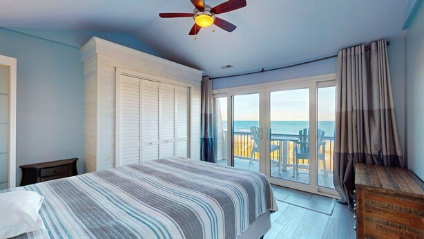 A bedroom with a bed, a ceiling fan, a sliding glass door to a balcony, and a view of the beach. - Pleasure Island Treasure Is an oceanfront townhome in a perfect location! (Carolina Beach)