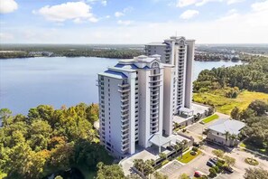 A high-rise building with multiple balconies, surrounded by a lake and greenery. - Trendy lake condo w/Disney view (Orlando)