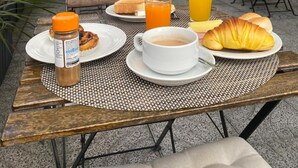 An outdoor dining area with a table set for breakfast, including croissants, toast, and juice, with a backdrop of bamboo plants and a wooden fence. - Hotel Residencial Dora (Braga)