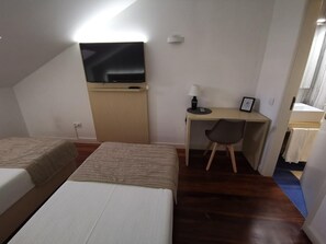 A hotel room with two beds, a desk with a chair, a television, and a bathroom visible through an open door. - Hotel Residencial Dora (Braga)