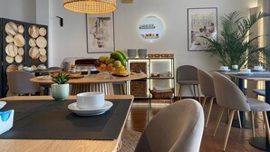 A modern dining area with a round table, chairs, a hanging light fixture, and a wall-mounted shelf with decorative items. - Hotel Residencial Dora (Braga)