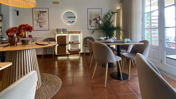 A modern dining area with a round table, chairs, a hanging light fixture, and a potted plant. - Hotel Residencial Dora (Braga)