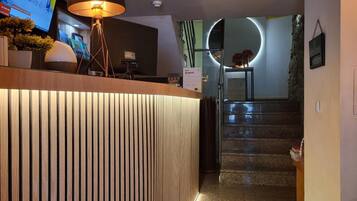 Un mostrador de recepción de diseño moderno, una escalera que sube a un nivel superior y una pantalla de televisión mostrando contenido.