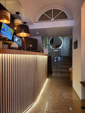 Un comptoir d’accueil au design moderne, un escalier menant à un niveau supérieur et un écran de télévision diffusant du contenu.