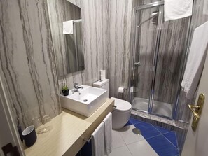 A bathroom with a marble wall, a sink, a toilet, and a glass-enclosed shower. - Hotel Residencial Dora (Braga)