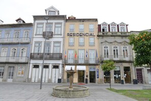 Una hilera de edificios con un edificio central identificado como 'RESIDENCIAL' y una fuente en primer plano.