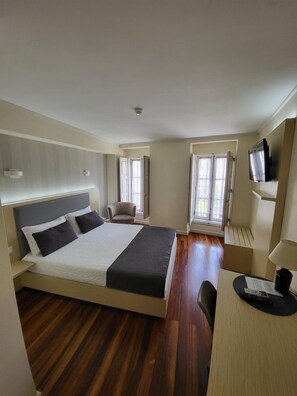 Una habitación de hotel con cama, escritorio, silla, televisor y ventana.
