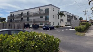 Un edificio residencial de varios pisos con balcones, un camino de entrada con reja y un coche estacionado.