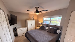 Un dormitorio con cama, ventilador de techo, televisión, armario y ventana con vistas.