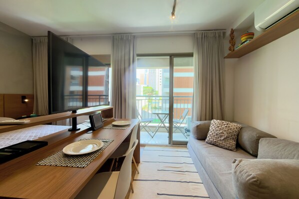 A modern hotel room with a wooden desk, a flat-screen TV, a sofa, and a balcony with a view of the city. - Apartment in Perdizes, 4th floor, with A/C, near Allianz Arena. (São Paulo)
