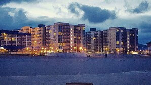 A beachfront hotel with multiple high-rise buildings, featuring balconies and illuminated windows. - 1-Bedroom Condo on the Ocean in Scenic Seaside with Fitness Room (Seaside)