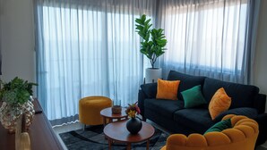 A modern living room with a dark sofa, yellow ottoman, and a potted plant. - Sky & Sea View (Mazatlán)