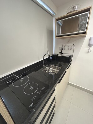 Cozinha com fogão por indução preto, pia de aço inoxidável e micro-ondas sobre a bancada.