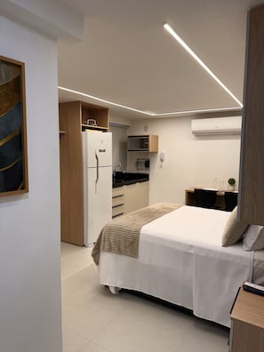Ein kleines Hotelzimmer mit Bett, Nachttisch und einer kompakten Küchenzeile.