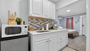A compact kitchen with white cabinetry, a microwave, a sink, and a small countertop area. - Simple & Comfy Tiny Pensacola Studio (Pensacola)