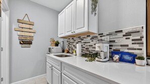 A kitchen with white cabinets, a tiled backsplash, and a coffee maker on the counter. - Simple & Comfy Tiny Pensacola Studio (Pensacola)