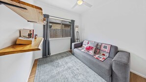 Uma sala de estar moderna com um sofá cinzento, uma estante de madeira, um ventilador de teto e uma janela com cortinas.