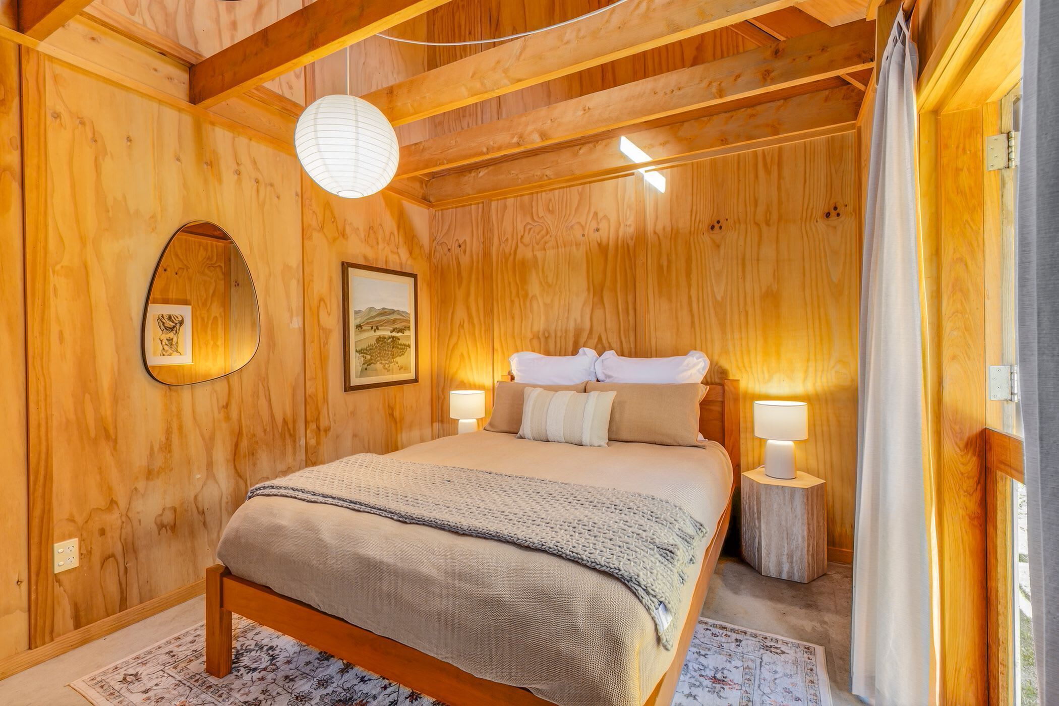 Une chambre à coucher aux murs lambrissés, avec un lit, deux lampes de chevet, un luminaire suspendu et un tableau encadré au mur.