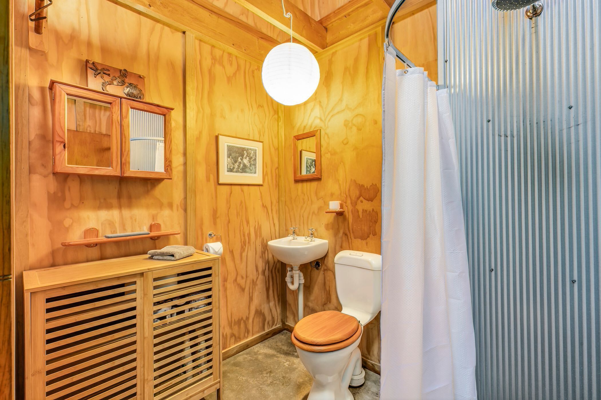 A wooden bathroom with a toilet, sink, and cabinets.