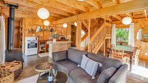 A cozy wooden cabin interior with a living area, kitchen, and dining space. - The Gatehouse - Tata Headlands (Wainui Bay)