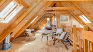 A cozy attic room with wooden beams, a round table, two chairs, a bed, and a large window. - The Gatehouse - Tata Headlands (Wainui Bay)