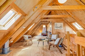 A cozy attic room with wooden beams, a round table, two chairs, a bed, and a large window. - The Gatehouse - Tata Headlands (Wainui Bay)